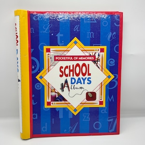 May include: A hardcover "School Days" album with a blue and red cover. The cover features the text "School Days Album" in a diamond shape, surrounded by pencils and other school-related graphics. The spine is yellow.