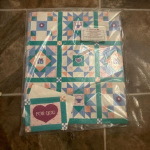 May include: A package of Current brand patchwork sampler gift wrap featuring a grid of squares with blue, pink, and teal geometric patterns, including small house, heart, and basket icons. A matching card with a purple heart and the text FOR YOU is included.