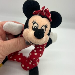 Puede incluir: Un coletero de peluche de Minnie Mouse con una cabeza de tela suave, orejas negras, un lazo rojo con lunares blancos y una banda el&aacute;stica a juego de color rojo con lunares blancos. El personaje tiene ojos, pesta&ntilde;as y nariz negra bordados.