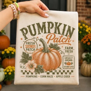 May include: A cream-colored canvas tote bag featuring a graphic print of a large orange pumpkin with green leaves and flowers. The text reads PUMPKIN Patch, FRESH FROM THE PATCH, FARM FRESH, LOCALLY GROWN, AUTUMN PICKED, PUMPKINS, CORN MAZE, APPLE CIDER.