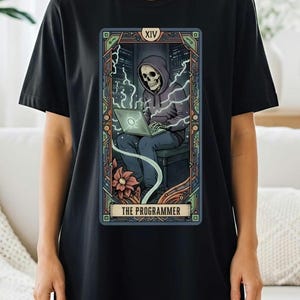 May include: Black t-shirt featuring a tarot card design. The card depicts a skeleton in a hoodie using a laptop, with the text "THE PROGRAMMER" at the bottom. The design has a colorful, intricate border and a floral element.