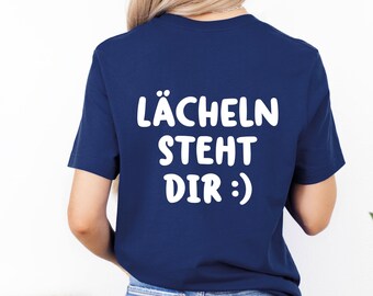 May include: A navy blue t-shirt with the German text "LÄCHELN STEHT DIR :)" in white, meaning "Smiling suits you." The shirt is a crew neck style and is being worn.