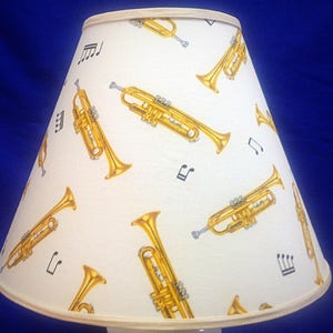 May include: A white lampshade with a pattern of gold trumpets and musical notes.
