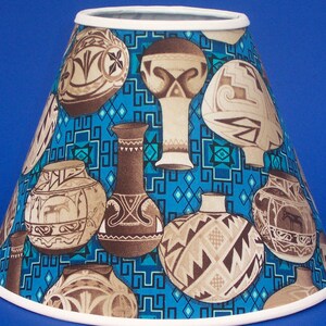 May include: A blue and brown lampshade with a Southwestern design featuring a repeating pattern of stylized pottery. The pottery is decorated with geometric designs and is set against a turquoise background.