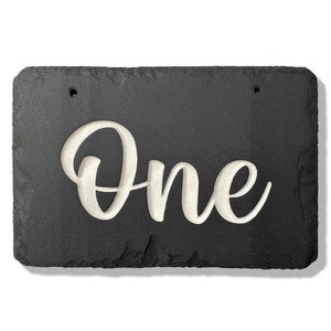 May include: Black slate sign with the word "One" carved in white lettering.