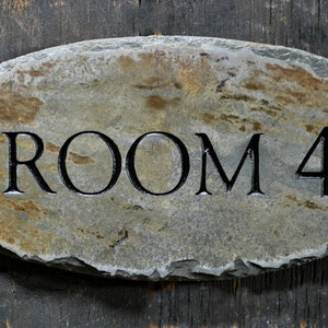 May include: A rustic oval-shaped slate sign with the text "ROOM 4" engraved in black lettering.