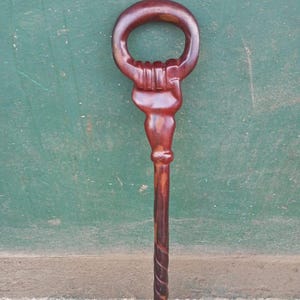 May include: A handcrafted wooden walking cane with a dark reddish-brown finish. The handle is a closed loop with a carved design, and the shaft features a spiral pattern. The cane is designed for support and mobility.