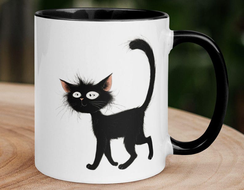 May include: White ceramic mug with a black interior, handle, and a whimsical black cat illustration. The cat has a fluffy appearance with pink-tipped ears and a long, curved tail. The mug is designed for hot beverages.