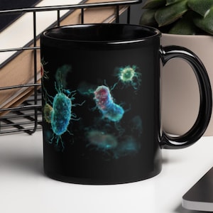 Puede incluir: Taza de cerámica negra con una colorida ilustración de varias bacterias y microorganismos. El diseño incluye células azules, verdes y rojas con detalles intrincados sobre un fondo negro. La taza tiene un asa curva y un acabado brillante.