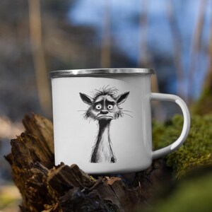 May include: White enamel mug with a silver rim and a whimsical black and white illustration of a sad, furry creature. The creature has large eyes and a long neck. The mug has a white handle.