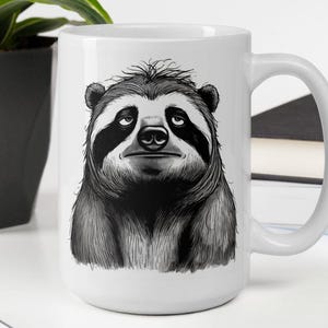 May include: White ceramic coffee mug featuring a detailed black and white illustration of a sloth's face. The sloth has a tired expression with dark circles around its eyes. The mug has a large handle for easy gripping.