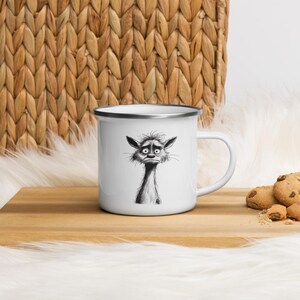 May include: White enamel mug with a black and white illustration of a cartoon creature with a worried expression. The mug has a silver rim and a white handle. The mug is on a wooden surface with cookies nearby.