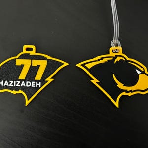 May include: Two yellow and black luggage tags. One tag features the number 77 and the name GHAZIZADEH. The other tag has a bear head design. Both tags have a clear plastic loop for attachment.