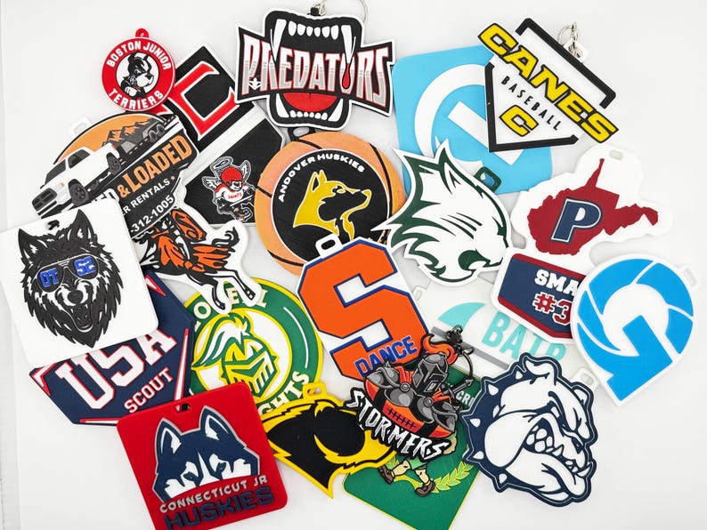 May include: A collection of various keychains with team logos and mascots. The keychains feature a variety of colors and designs, including a wolf wearing sunglasses, a bulldog, and the text "PREDATORS".