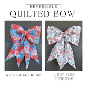 May include: Reversible quilted bow with two distinct designs. One side features a watercolor bird pattern with red, blue, and white hues. The other side showcases a light blue patriotic design with American flags and stars. The text "Reversible Quilted Bow" is at the top.