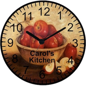 May include: A round clock with a black frame and Roman numeral markings. The clock face is a vintage-style image of a bowl of red apples with the text "Carol's Kitchen" below the bowl.