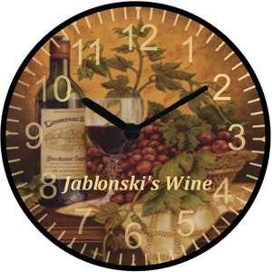 May include: A round clock with a black frame and gold Roman numeral hour markers. The clock face features a still life image of a bottle of wine, a glass of red wine, and grapes. The text "Jablonski's Wine" is printed on the clock face.