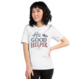 May include: A white short-sleeved t-shirt featuring the text His GOOD HELPER in blue and maroon lettering. A small illustration of a diamond ring is positioned next to the word His, and the text GENESIS 2:18 is printed below with two small rings.
