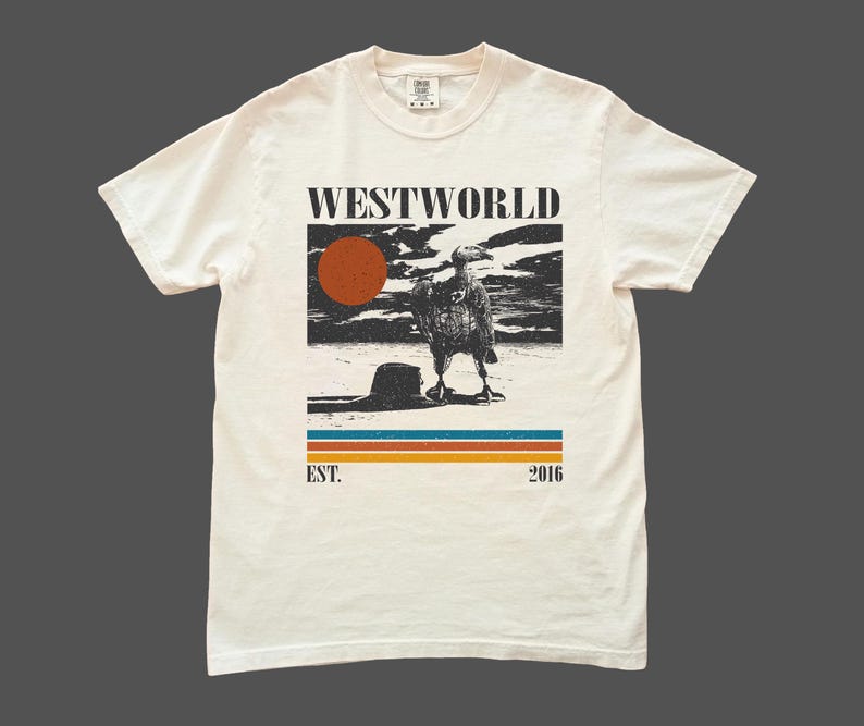 May include: Off-white t-shirt with a graphic print featuring the word "WESTWORLD" above a desert scene with a bird and a setting sun. Below the image are horizontal stripes and the text "EST. 2016".