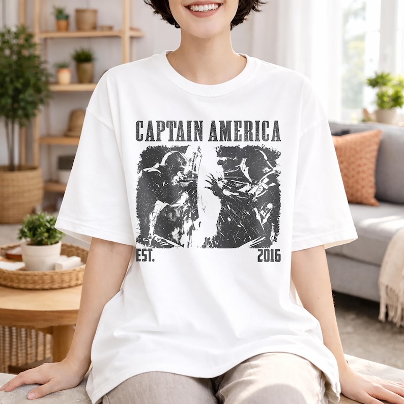 May include: White t-shirt featuring a black and white graphic of Captain America. The shirt has the words "CAPTAIN AMERICA" printed across the top, with "EST. 2016" below the graphic. The shirt is a casual, oversized fit.
