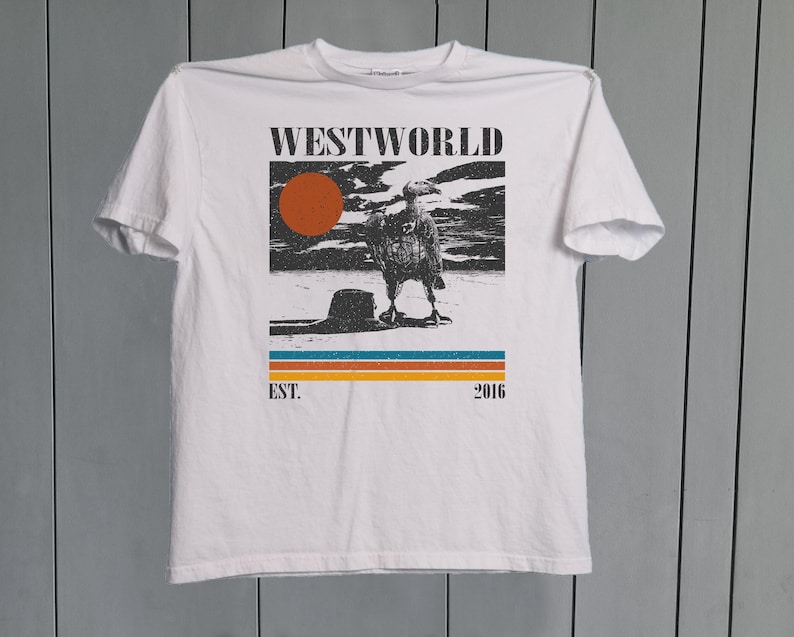 May include: White t-shirt with a graphic design featuring the word "WESTWORLD" above an illustration of a bird and a sunset. Below the image are the words "EST. 2016" and a series of horizontal stripes.