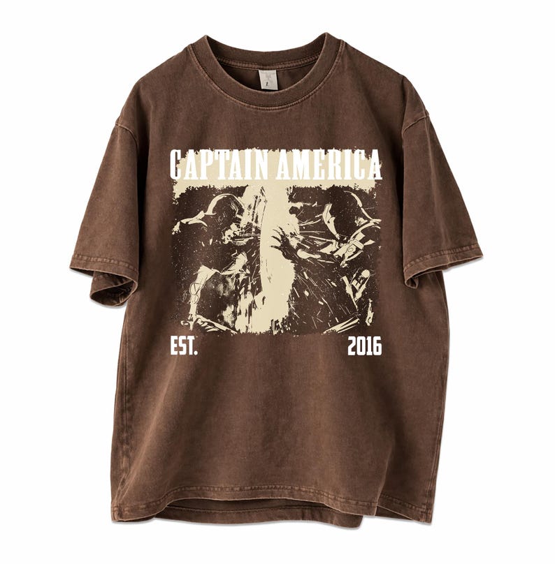 May include: Brown t-shirt featuring a graphic of Captain America with the text "CAPTAIN AMERICA" above the image and "EST. 2016" below. The graphic is in black and white, with a vintage, distressed look. The shirt has short sleeves and a crew neck.