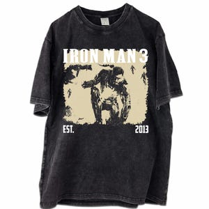 May include: Dark grey t-shirt with a distressed graphic of Iron Man from Iron Man 3. The design includes the text "IRON MAN 3" above the image and "EST. 2013" below. The shirt has a vintage, worn appearance.