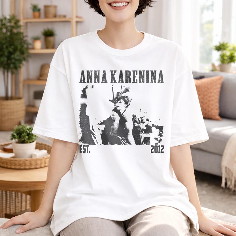 Puede incluir: Camiseta blanca con un gr&aacute;fico en blanco y negro de una mujer con sombrero, con el texto "ANNA KARENINA" arriba y "EST. 2012" abajo. La camiseta tiene un corte holgado.