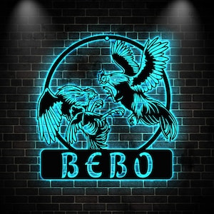 Puede incluir: Una pieza de arte mural de metal negro que representa tres gallos luchando, enmarcados por un círculo y una base rectangular. El diseño se destaca con un brillo de neón azul brillante, sobre un fondo de pared de ladrillo oscuro. La palabra "BEBO" se muestra en la base.