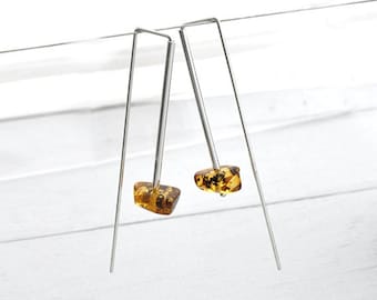 May include: A pair of drop earrings featuring long, thin silver-toned metal bars with a rectangular, geometric shape. Each earring is finished with a small, polished, translucent amber-colored stone at the base, displaying natural inclusions.