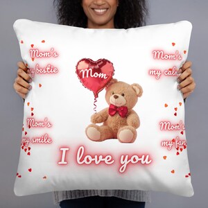 Puede incluir: Cojín blanco con un oso de peluche sosteniendo un globo rojo en forma de corazón con "Mamá". El cojín tiene el texto "Mom's my bestie", "Mom's my smile", "Mom's my calm", "Mom's my fan" y "I love you".