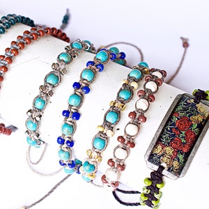 May include: A set of six colorful bracelets with various beads and charms. The bracelets are made with different materials, including turquoise, brown, white, and green beads. One bracelet features a rectangular charm with a floral design.