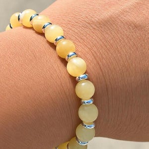May include: A stretch bracelet featuring alternating round, pale yellow beads and small, polished silver-toned metal spacers. The beads have a smooth, semi-translucent finish, and the bracelet is designed to fit snugly around the wrist.