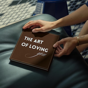 May include: A square, dark brown hardback book with the white text THE ART OF LOVING you printed on the front cover. The title features a mix of bold sans-serif lettering for the first three words and a delicate, cursive script for the final word.