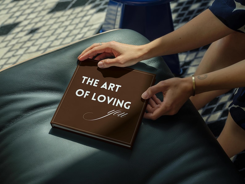 May include: A square, dark brown hardback book with the white text THE ART OF LOVING you printed on the front cover. The title features a mix of bold sans-serif lettering for the first three words and a delicate, cursive script for the final word.