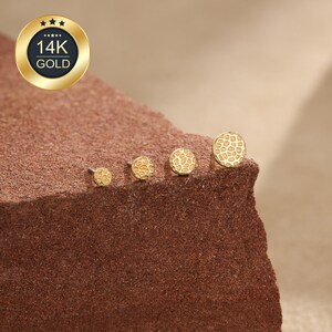 May include: Four round 14K gold stud earrings arranged in a row by size, each featuring a textured honeycomb pattern on the surface. The earrings are displayed in a line, showcasing a consistent design across the different diameters of the studs.