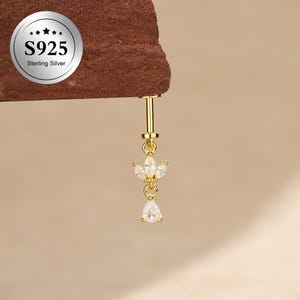 May include: A gold-toned S925 sterling silver body jewelry piece featuring a vertical post with a dangling charm. The charm consists of three marquise-cut clear stones arranged in a fan shape above a single pear-cut clear stone drop.