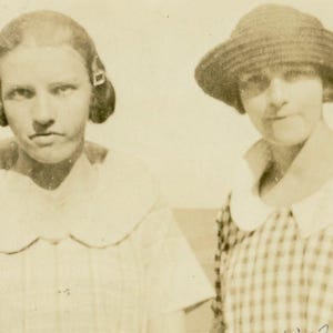 Peut inclure: Deux femmes sur une photo en noir et blanc. La femme de gauche porte une chemise blanche à col avec un col festonné. La femme de droite porte un chapeau et une robe à carreaux avec une chemise blanche à col.