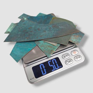May include: A pile of irregularly shaped, weathered copper pieces with blue-green patina, weighing 0.50 lb, are displayed on a digital scale. The scale has a silver surface and a digital display.