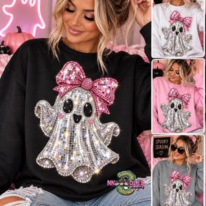 May include: A black crewneck sweatshirt featuring a large graphic of a ghost covered in reflective silver mirror tiles. The ghost has black oval eyes, small pink heart-shaped cheeks, and a large, bright pink glittery bow on its head.