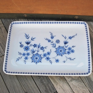 May include: Rectangular white ceramic serving platter with a blue floral design. The platter features a border of small blue dots and a central arrangement of blue flowers and leaves. A decorative piece for serving food.