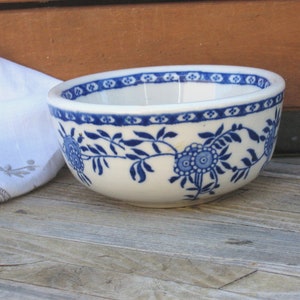 May include: A small white ceramic bowl with a blue and white floral pattern. The bowl has a simple design with a blue floral border and a blue floral pattern in the center.