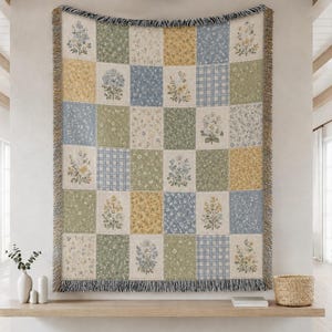 May include: A woven throw blanket featuring a patchwork grid of squares in muted shades of sage green, dusty blue, and soft yellow. The design includes floral bouquets, small wildflower patterns, and a classic gingham check, finished with fringed edges.