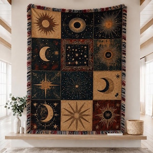 May include: A woven throw blanket featuring a grid of twelve rectangular panels displaying celestial motifs including suns, moons, and stars in shades of gold, deep blue, and dark red. The blanket has a fringed edge with multi-colored threads.