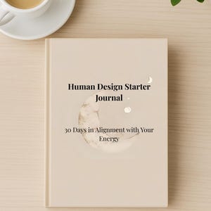 May include: A beige journal titled "Human Design Starter Journal" with the subtitle "30 Days in Alignment with Your Energy." The cover features a crescent moon and stars design. A cup of coffee sits on a white saucer in the upper left corner.