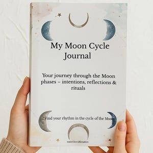 Könnte beinhalten: Ein Journal mit dem Titel "My Moon Cycle Journal" wird von Händen gehalten. Das Cover zeigt Halbmond-Illustrationen und den Text "Your journey through the Moon phases - intentions, reflections & rituals."