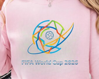 Puede incluir: Sudadera rosa claro con un gráfico colorido de un balón de fútbol dentro de una red de líneas. El texto "FIFA World Cup 2026" está impreso debajo en azul.