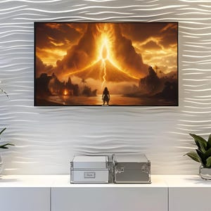 May include: A framed digital art print depicting a volcanic eruption with a figure standing in the foreground. The artwork features a fiery color palette of oranges, yellows, and browns, with a dramatic lightning strike. The print is displayed on a white textured wall.