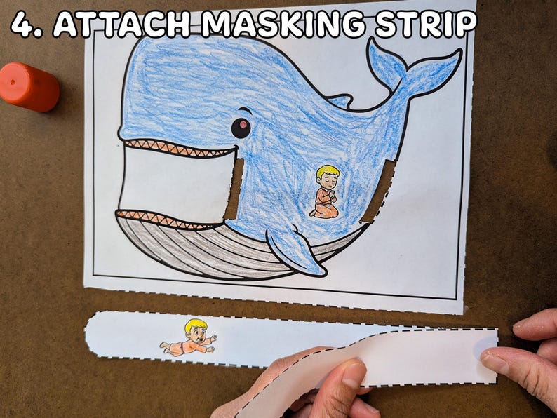 May include: A blue whale coloring page with a small figure inside, and the text "4. ATTACH MASKING STRIP" at the top. A person is holding a white strip with a drawing of a small figure.
