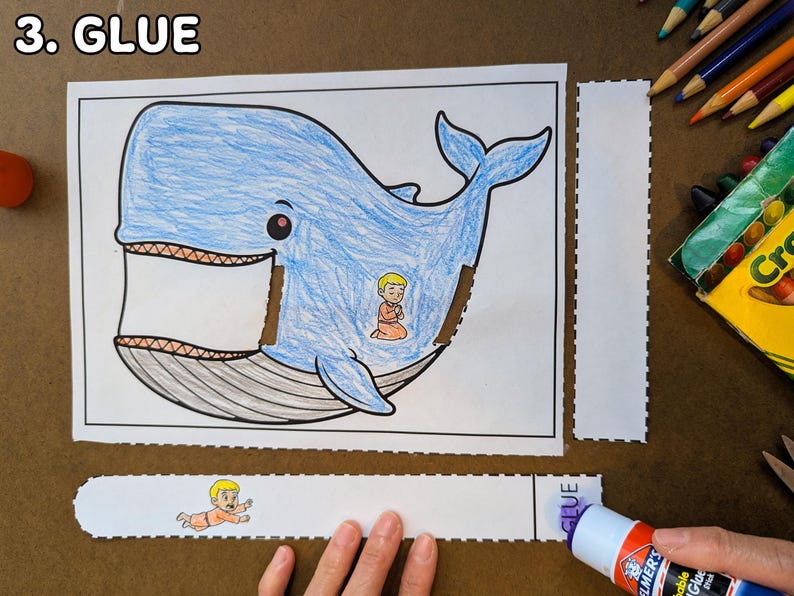 May include: A blue whale coloring page with a small figure inside, along with cut-out pieces and a glue stick. The text "3. GLUE" is at the top left. Crayons and scissors are in the background.